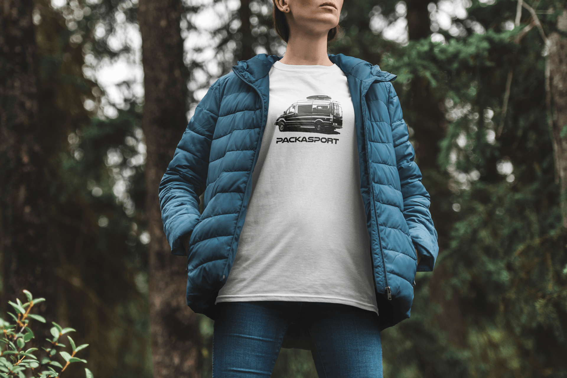 A woman wearing a blue jacket and a white t-shirt is standing in the woods.
