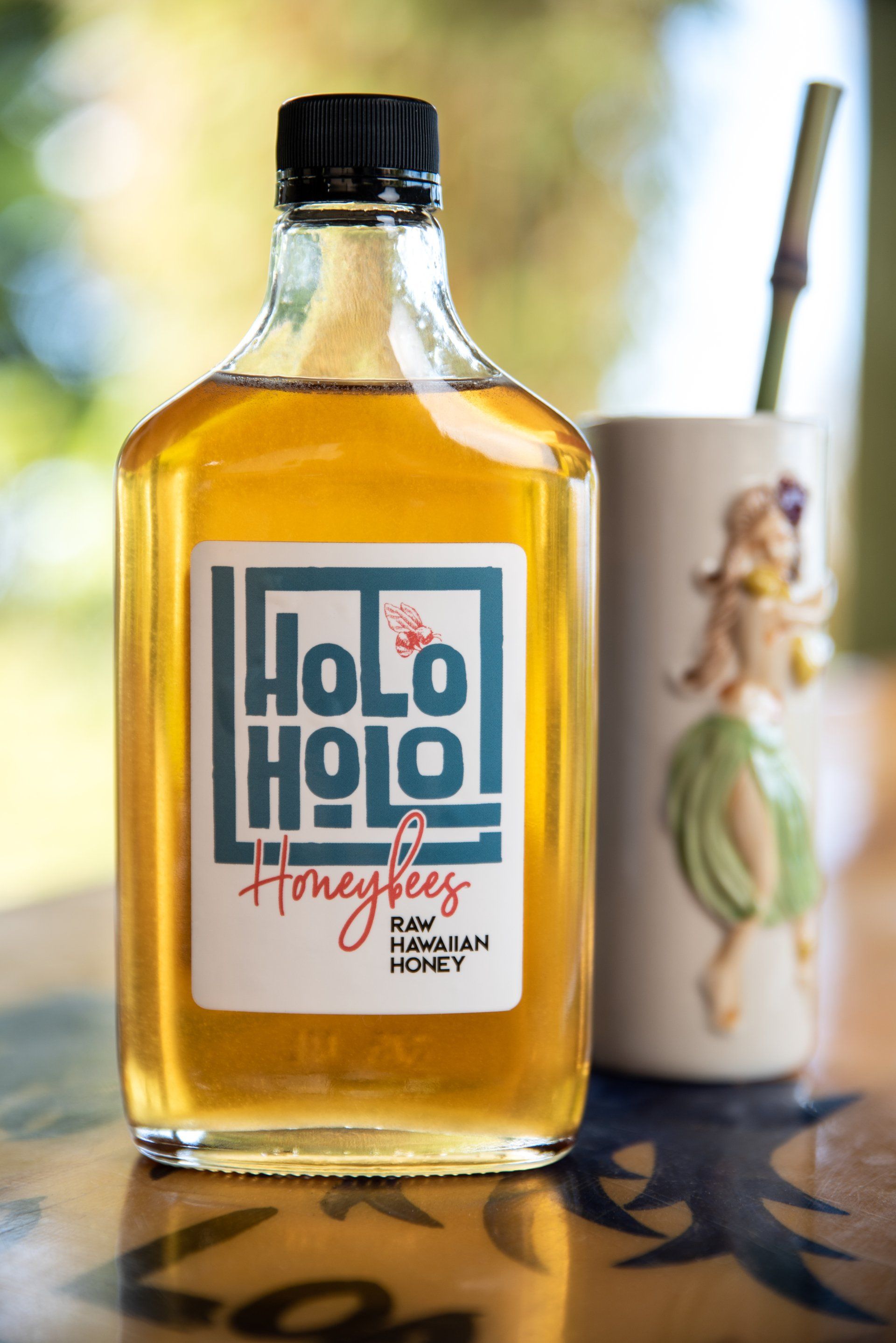 A bottle of  Holoholo Honey next to a cup with a hula girl on it .