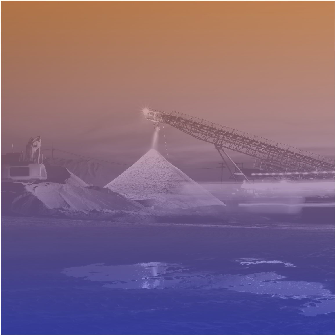 A conveyor belt deposits material into a large pile at an industrial site, with a sunset sky overhead.