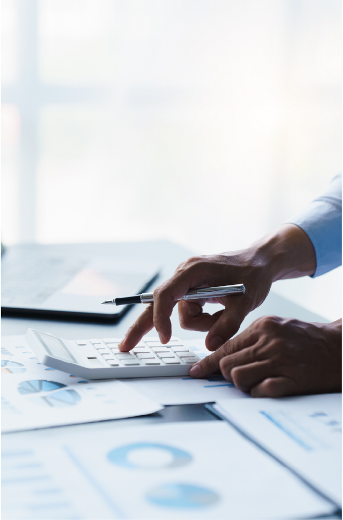 Hands use a calculator and pen to analyze financial charts on a desk in a brightly lit office.