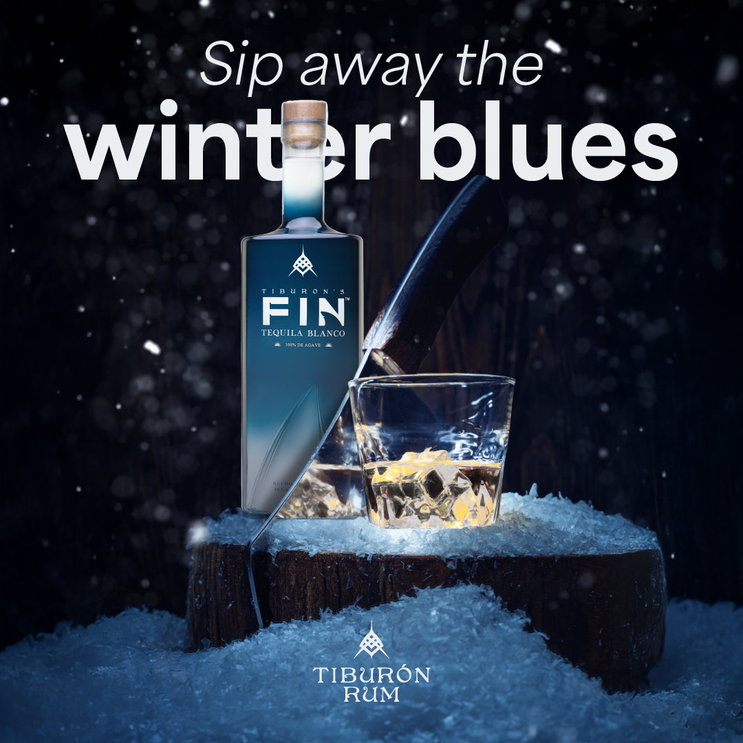 A bottle of Tiburon Fin rum next to a glass of rum with ice on a snowy log, with the text 