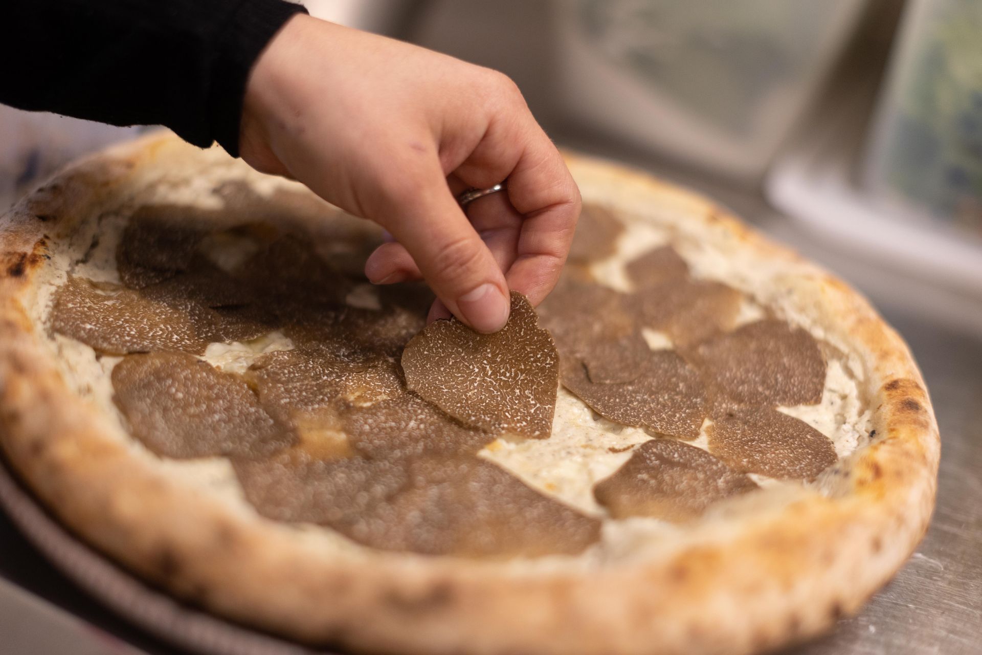 Une personne met des tranches de truffes sur une pizza.