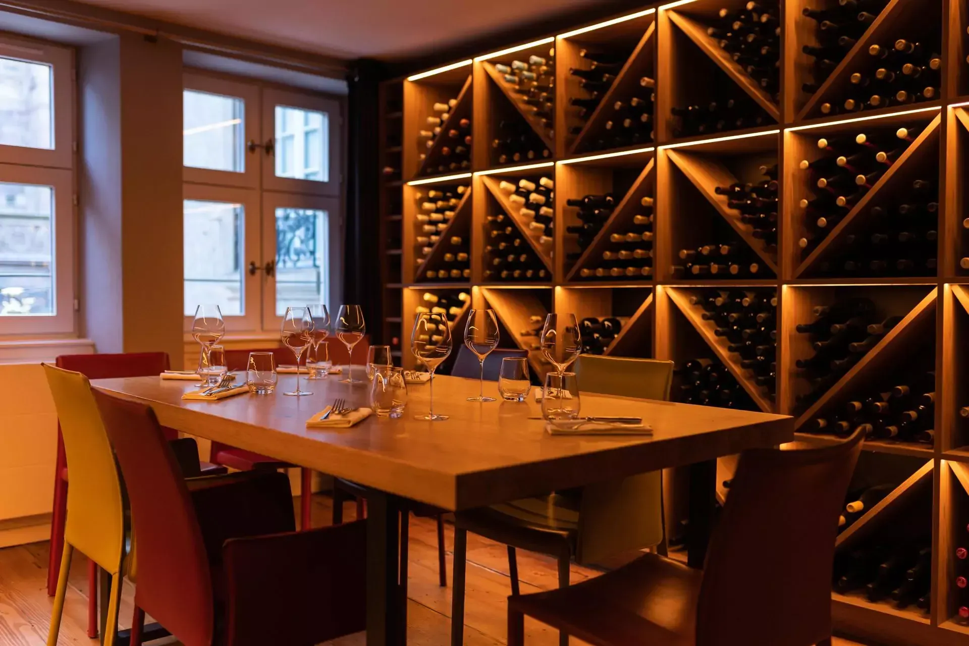 Une salle à manger avec une table et des chaises devant un mur de bouteilles de vin.