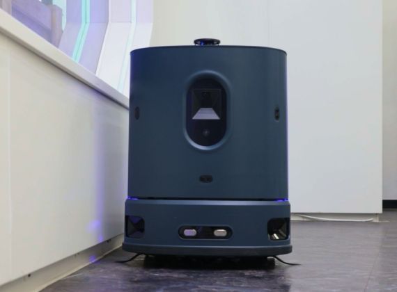 Dark teal cleaning robot against a white wall, in a modern interior.