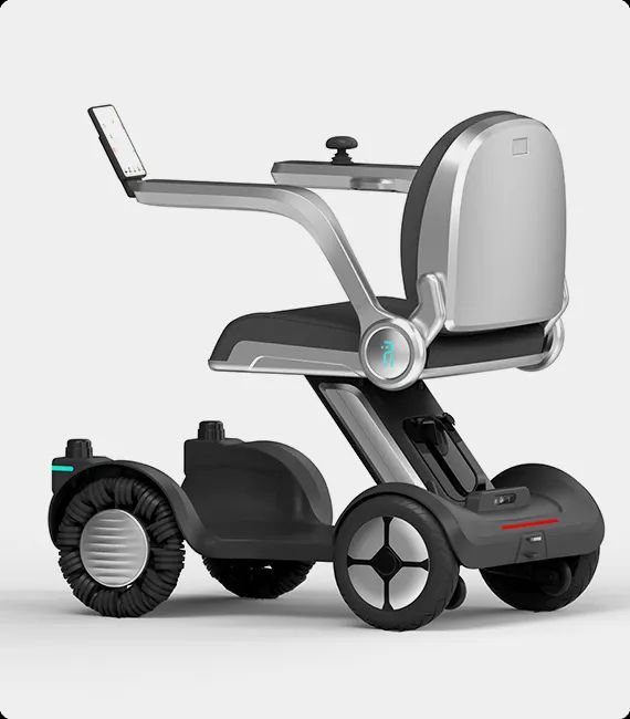 A modern, silver and black electric wheelchair. It has a digital display, armrests and a single rear wheel.