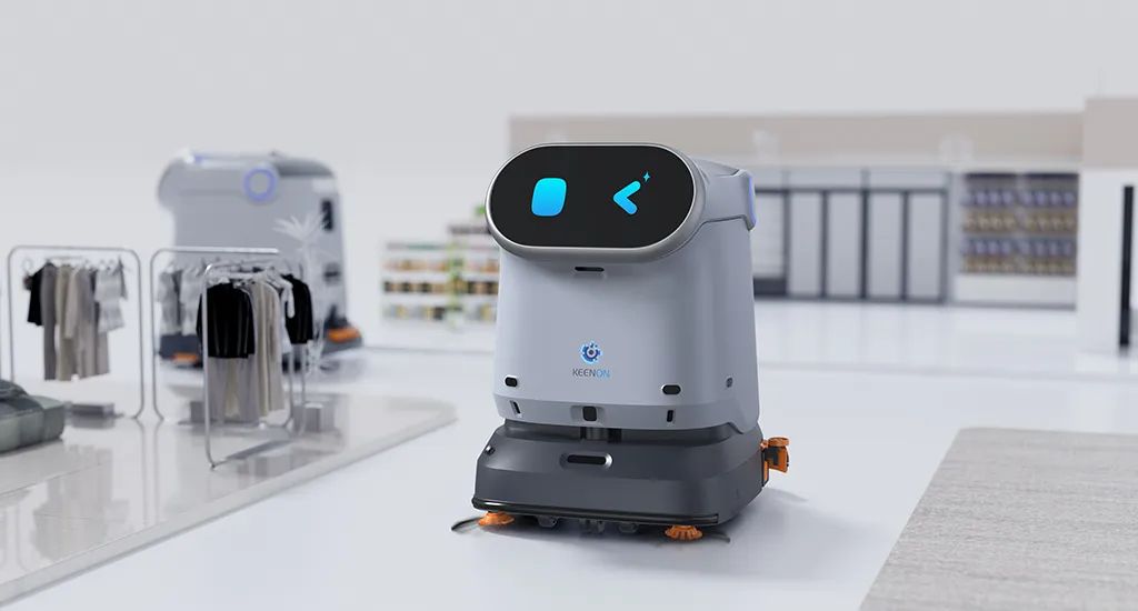 A gray service robot with a blue screen face in a retail store setting. Another robot and racks of clothes are visible.