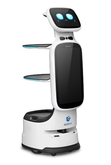 White service robot with shelves, blue eyes on screen, standing on a gray platform in front of a gray background.