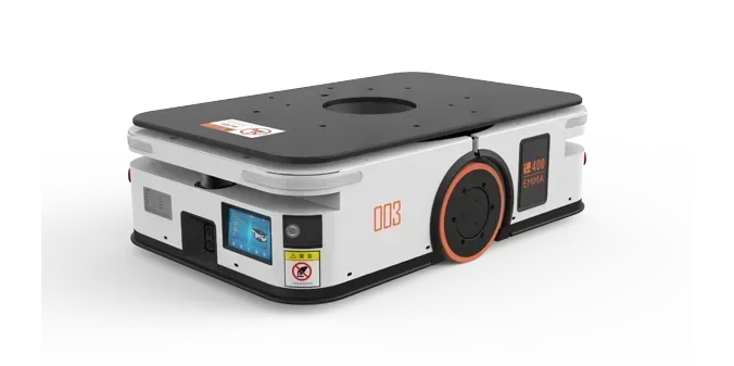 Person in hardhat pushing a robotic cart with a box in a warehouse aisle.