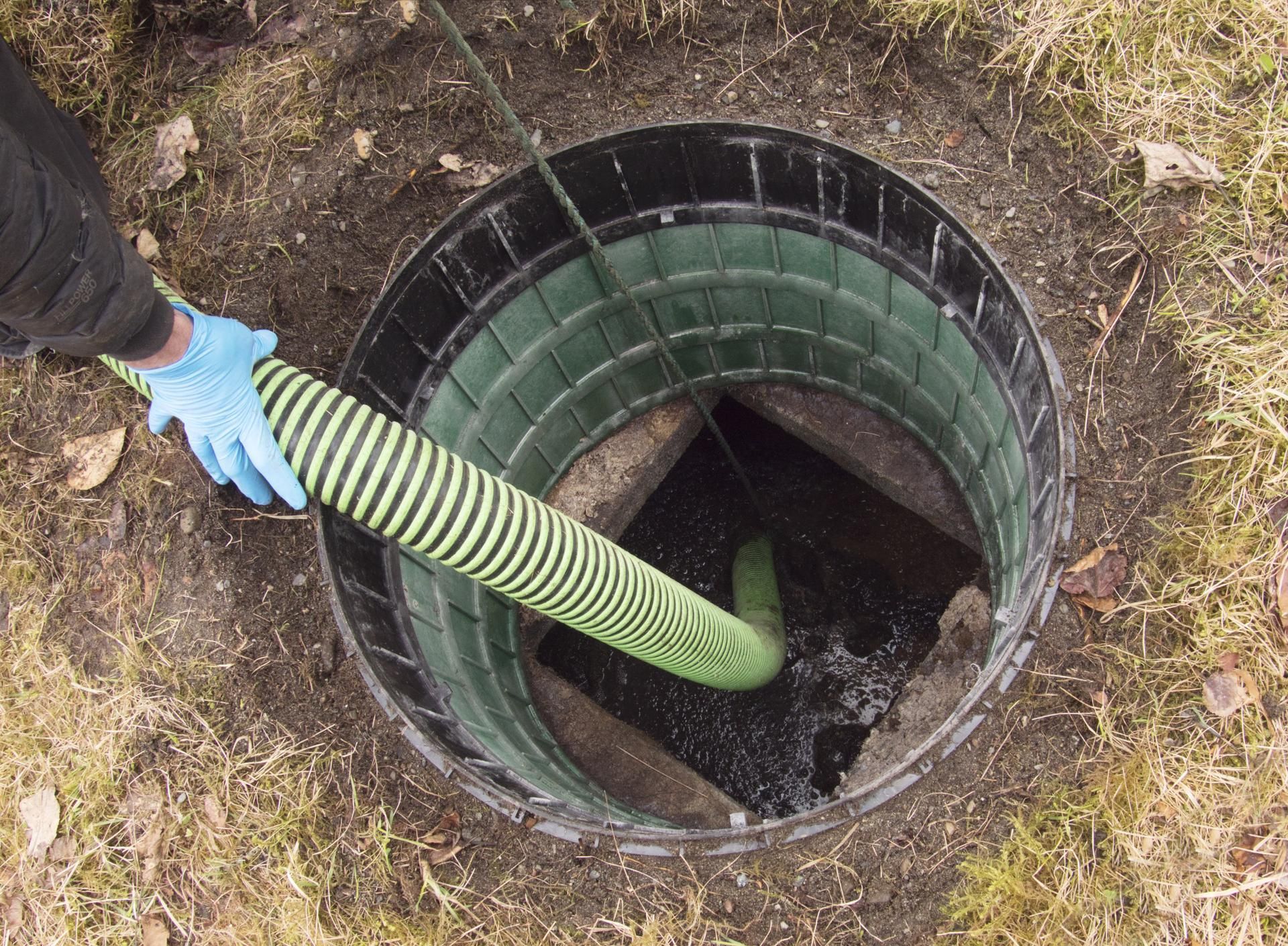A person is pumping water into a septic tank with a green hose.