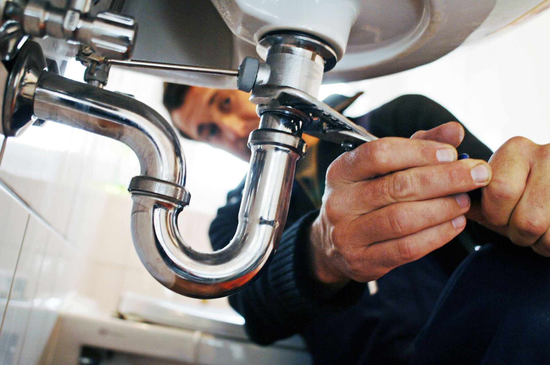Plumber in a blue uniform, repairing sink drain with wrench, showcasing expert plumbing services.