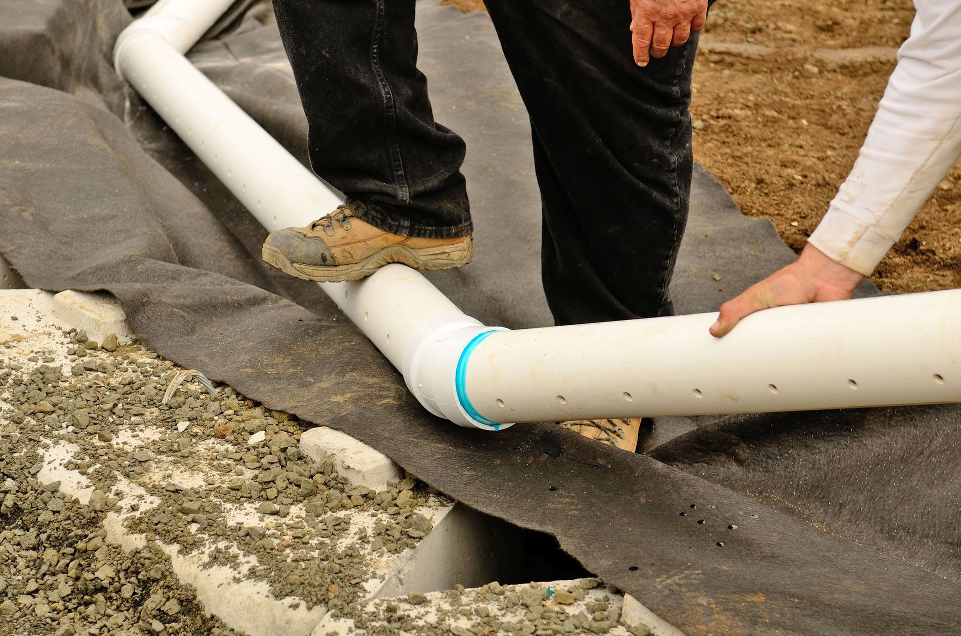 A man is working on a drain pipe in the dirt.