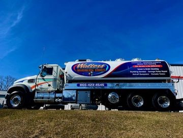 A white and purple tanker truck is parked in a grassy field.