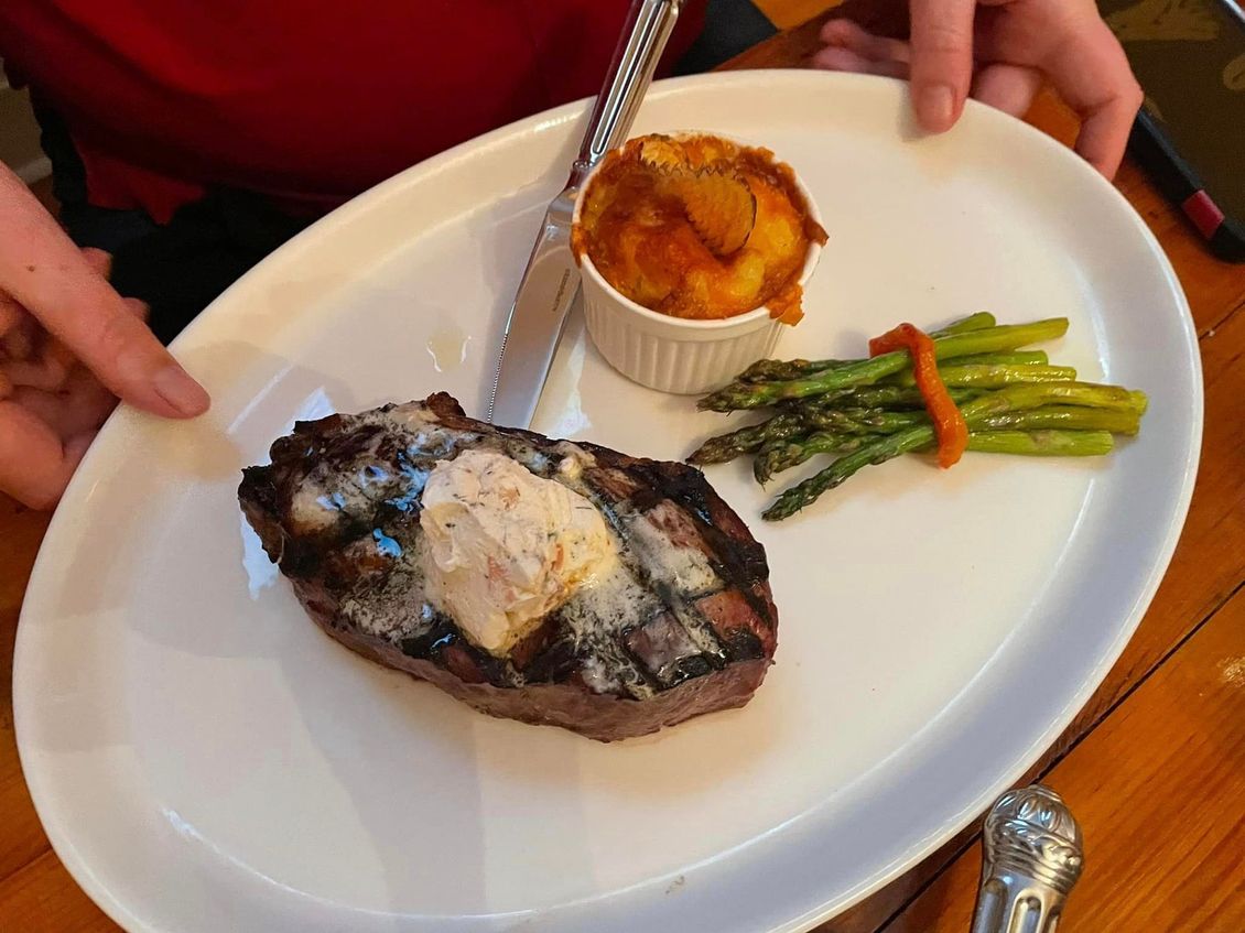 A person is cutting a steak on a plate with asparagus and mashed potatoes.