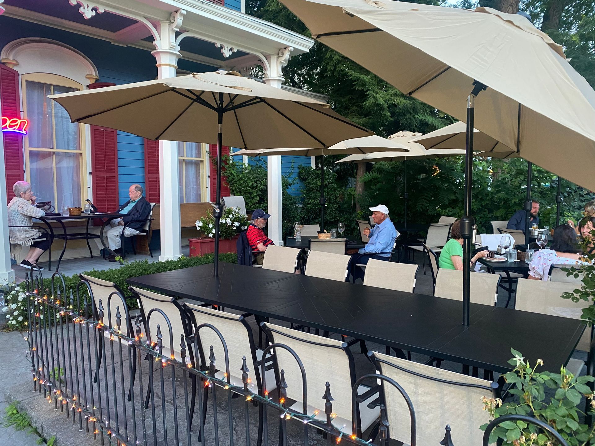 A group of people are sitting at tables under umbrellas outside of a restaurant.