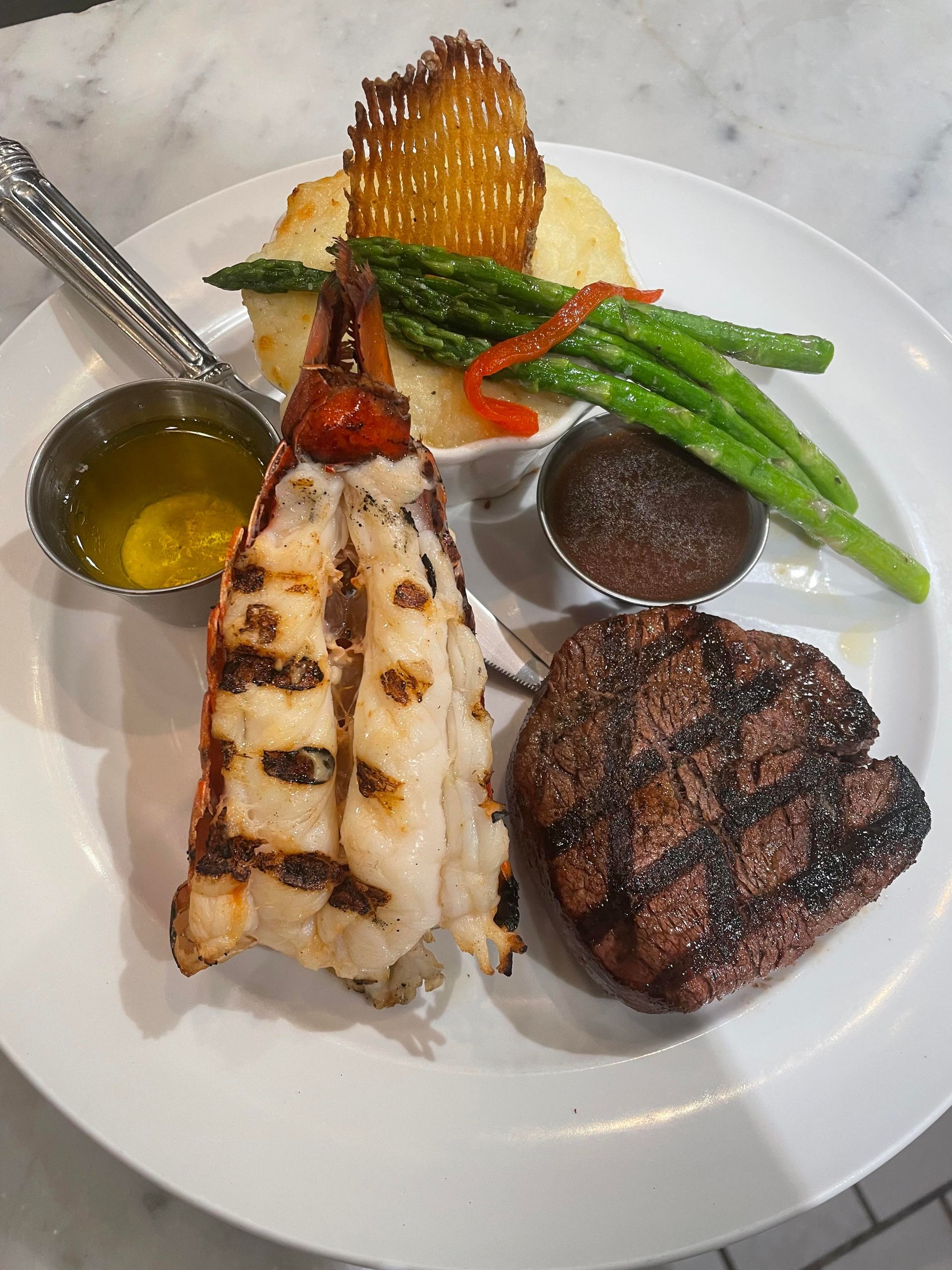 A white plate topped with a steak , lobster tail , mashed potatoes and asparagus.