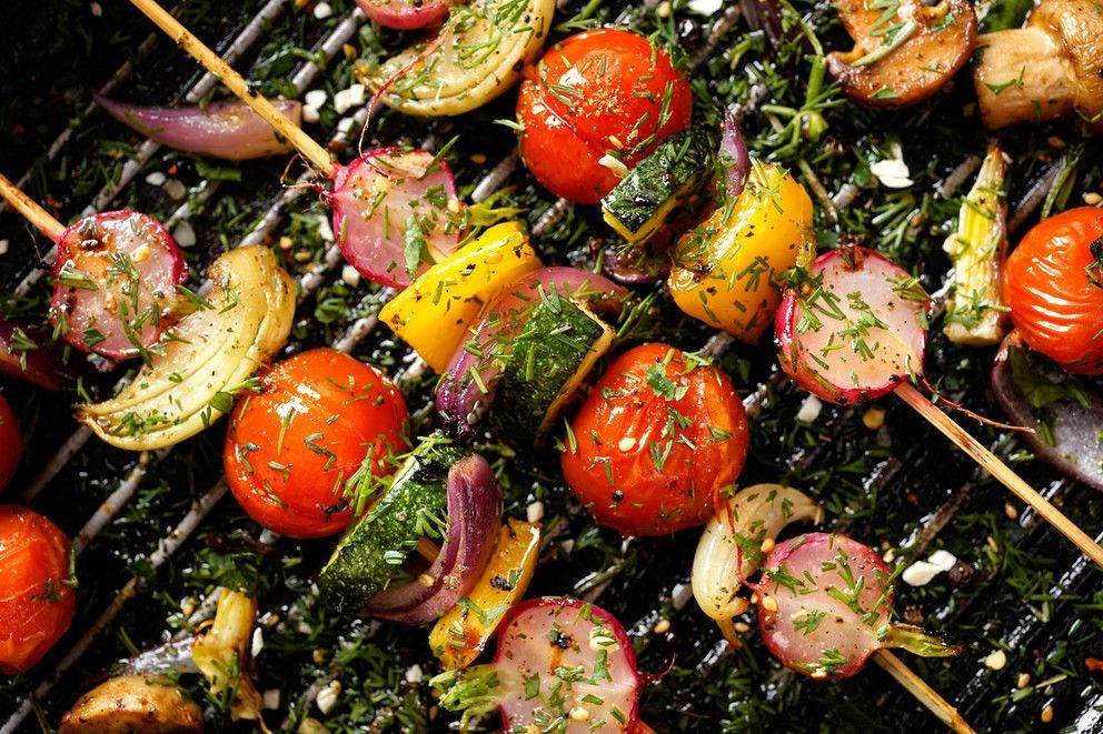 Grilled vegetable skewers on a grill, featuring tomatoes, bell peppers, onions, mushrooms, and zucchini seasoned with herbs.