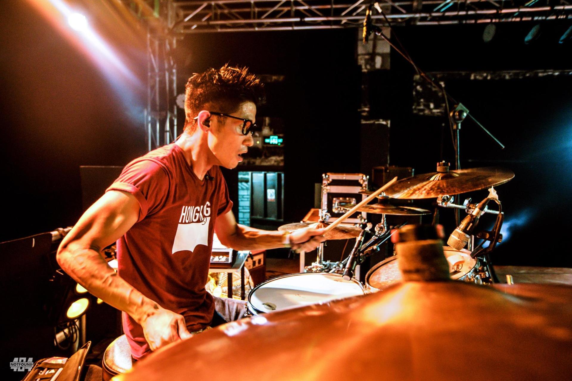 A man in a red shirt is playing drums on a stage.