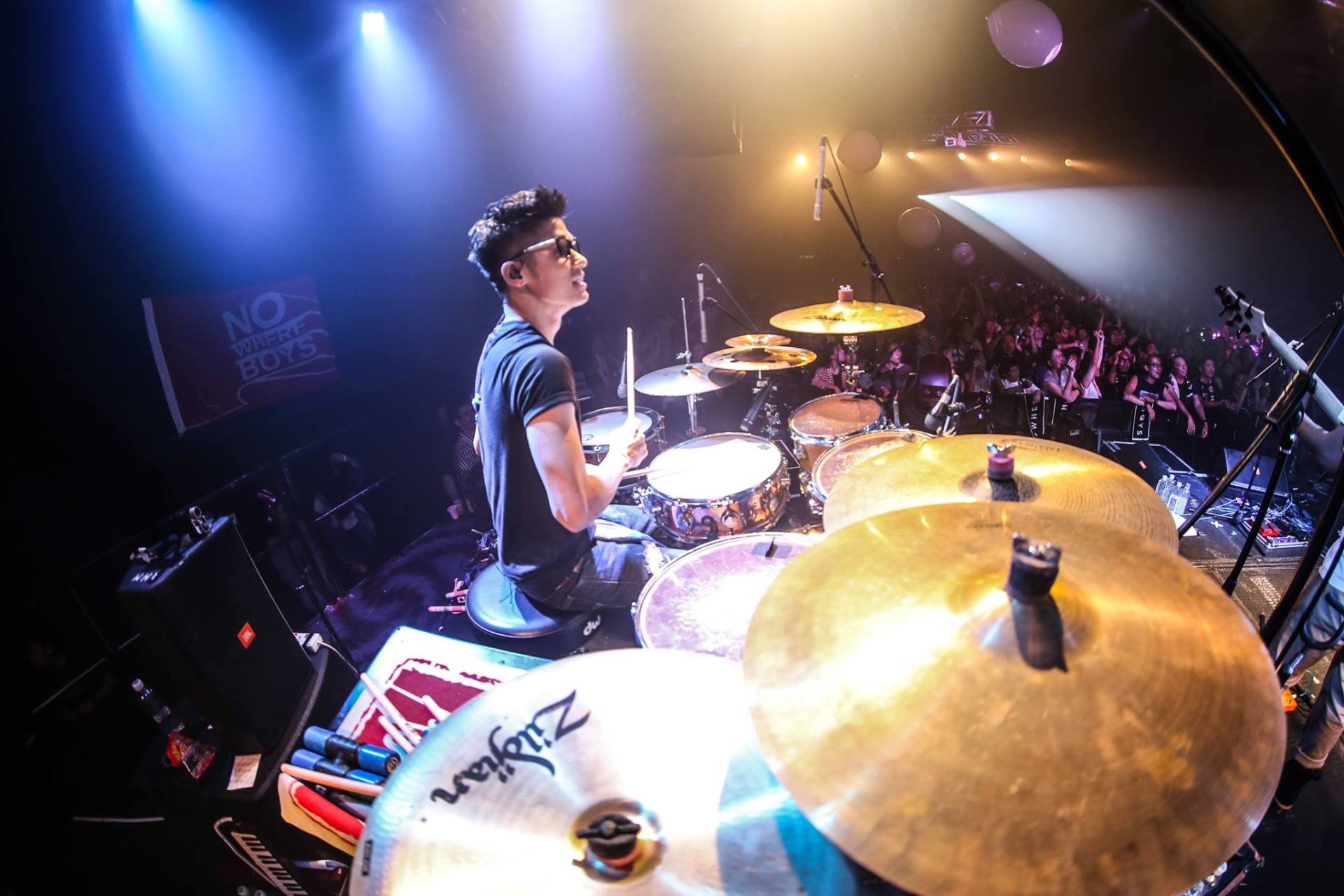 A man is playing drums on a stage in front of a crowd.