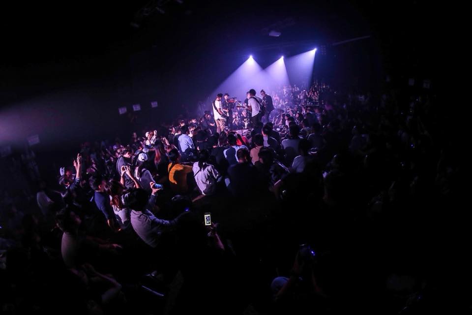 A crowd of people are standing in a dark room at a concert.