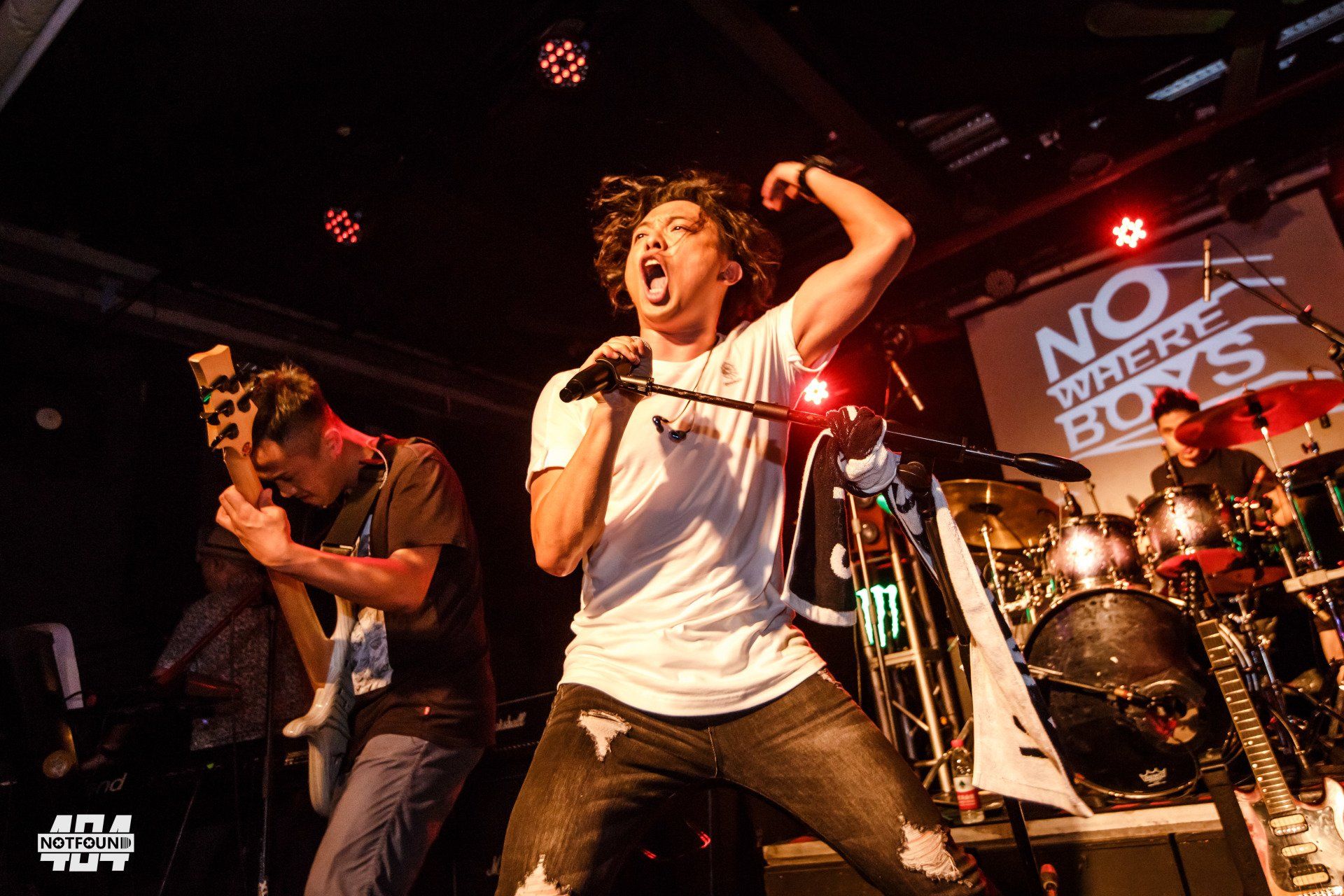 A man singing into a microphone in front of a sign that says no where boys