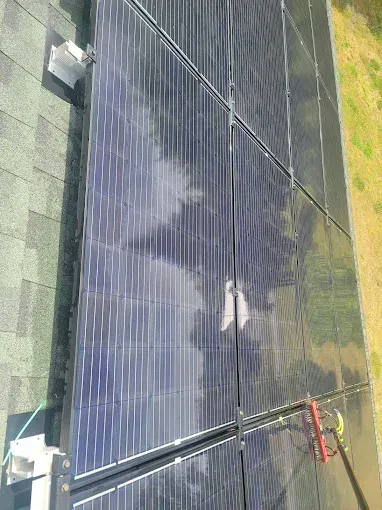 Solar panels on a roof, reflecting the sky. A cleaning tool rests against the panels.
