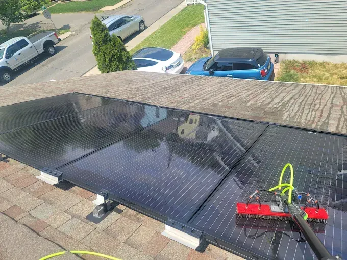 Solar panels on a rooftop being cleaned with a brush. Cars are parked on the street.