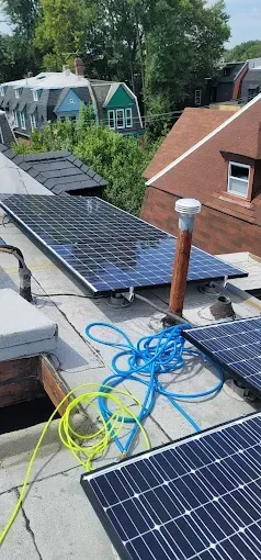 Solar panels on a rooftop with blue and yellow wires. Houses and trees are in the background.