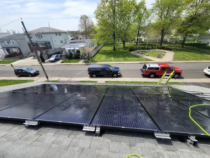 Solar panels on a roof, being cleaned. Red truck, blue SUV, and black car parked nearby.