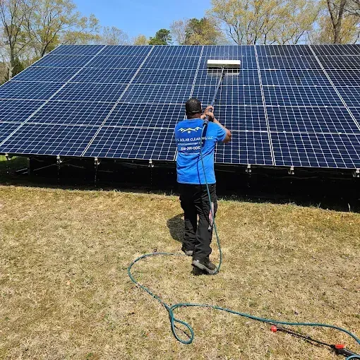 Person cleaning solar panels with a long-handled brush. Blue shirt, black pants, outdoor setting.