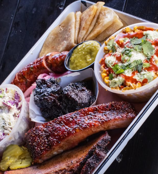 A tray of food including ribs coleslaw and corn on the cob