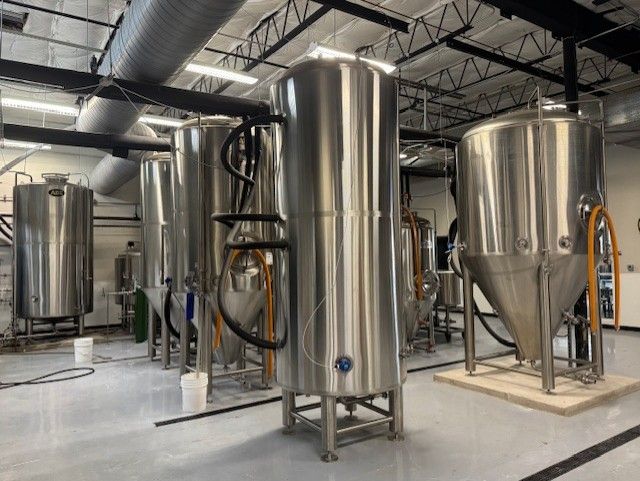 A row of stainless steel tanks are lined up in a room.