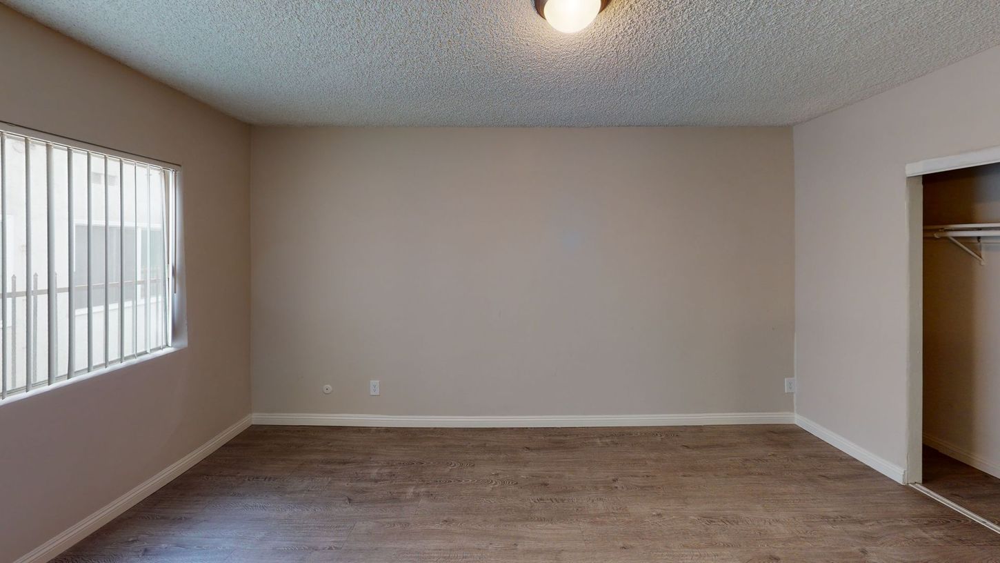 Empty room with brown flooring, beige walls, a window with blinds, and a closet.