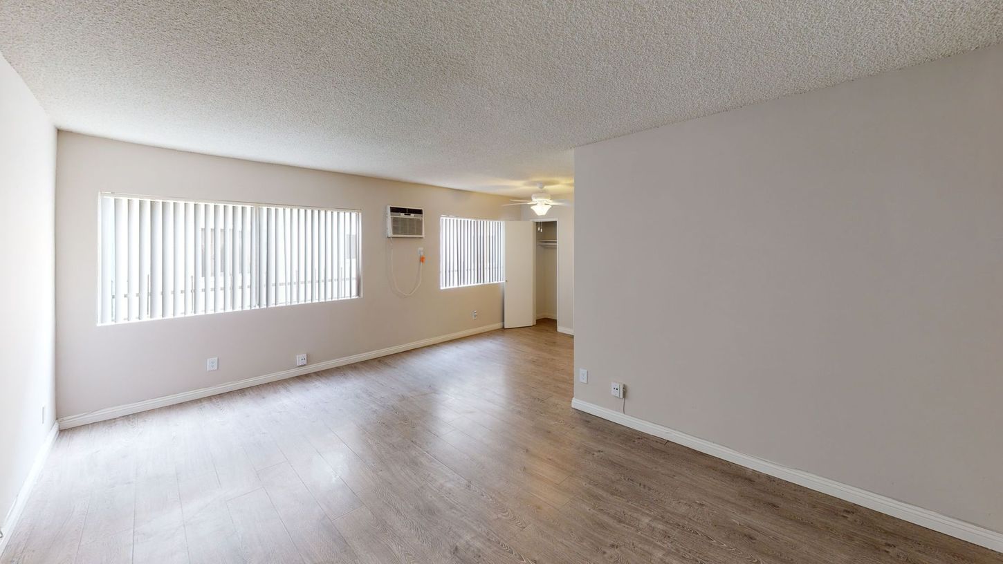 Empty living room with wood-look flooring, white walls, two windows with blinds, and a popcorn ceiling.
