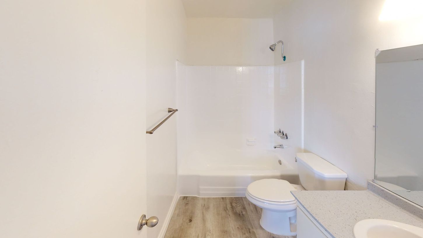White bathroom with a shower, toilet, and vanity. Gray wood-look flooring.