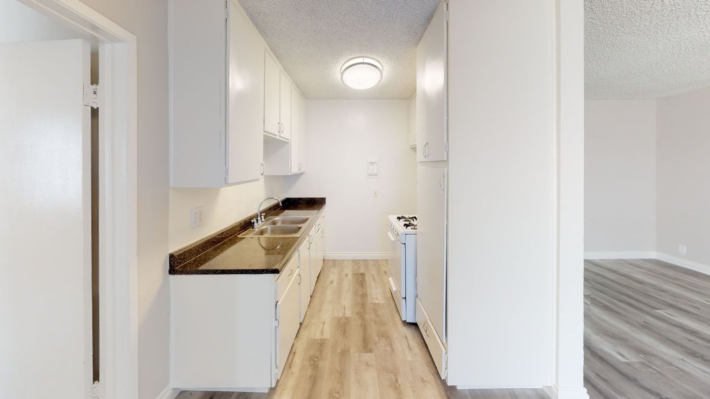 Narrow kitchen with white cabinets, dark countertop, and wood-look flooring.