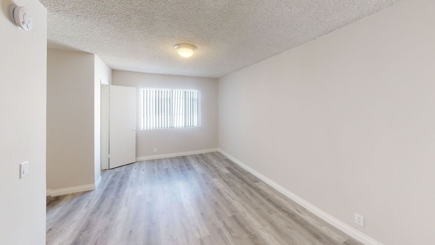 Empty room with gray wood-look flooring, white walls, window with blinds, and a light fixture.