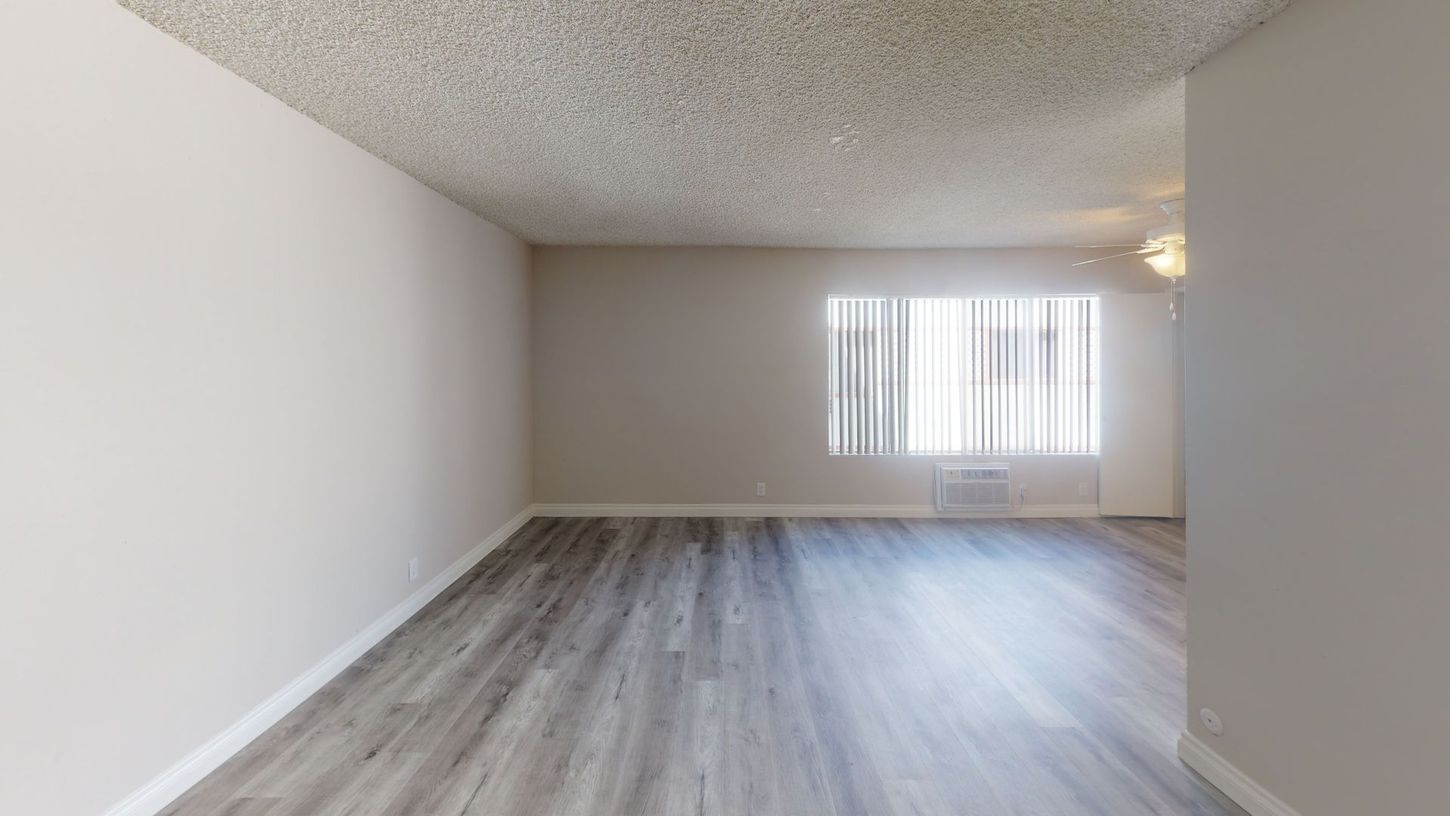 Empty living room with wood-look flooring, light walls, and a window with blinds.
