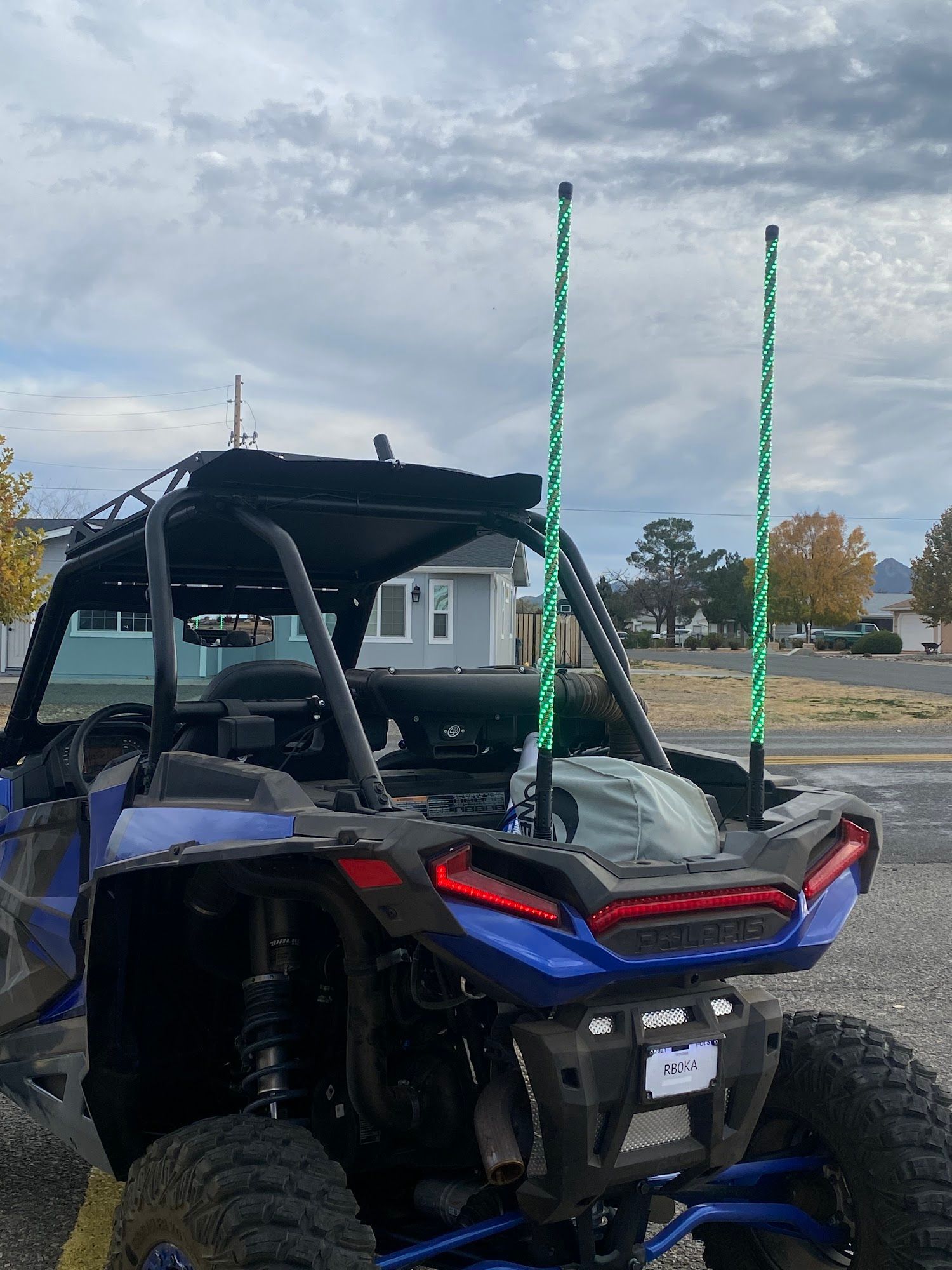 Blue and black side-by-side all-terrain vehicle with two green LED whips against a cloudy sky.