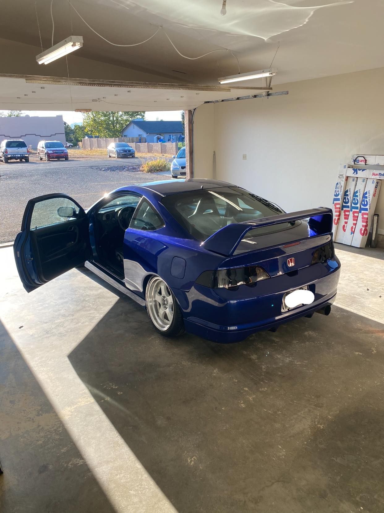 Blue sports car with open door parked inside a garage. Sunlight streams in, illuminating the car and surrounding area.