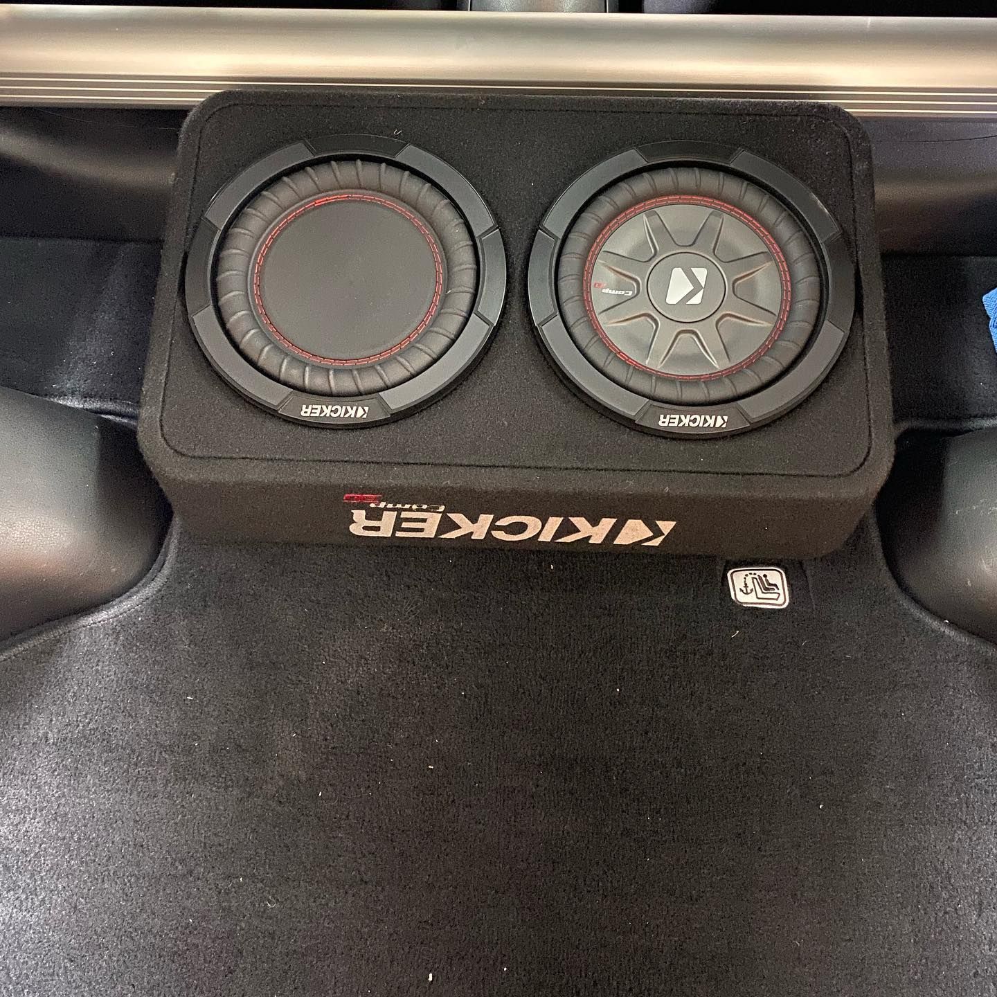 A black Kicker subwoofer enclosure with two speakers in the trunk of a car. The speakers have red accents.