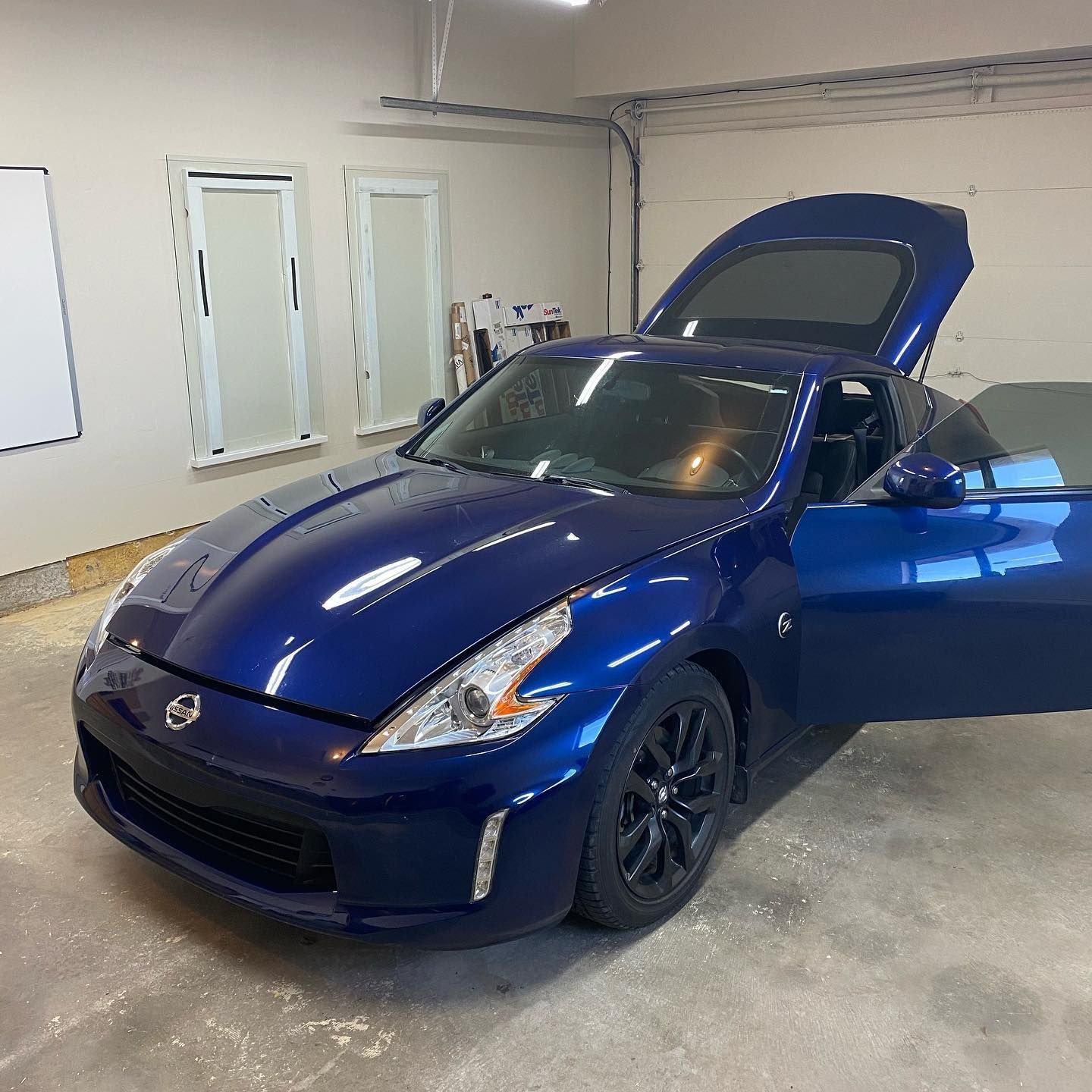 A blue Nissan 370Z sports car with its doors and hatch open, parked inside a garage.