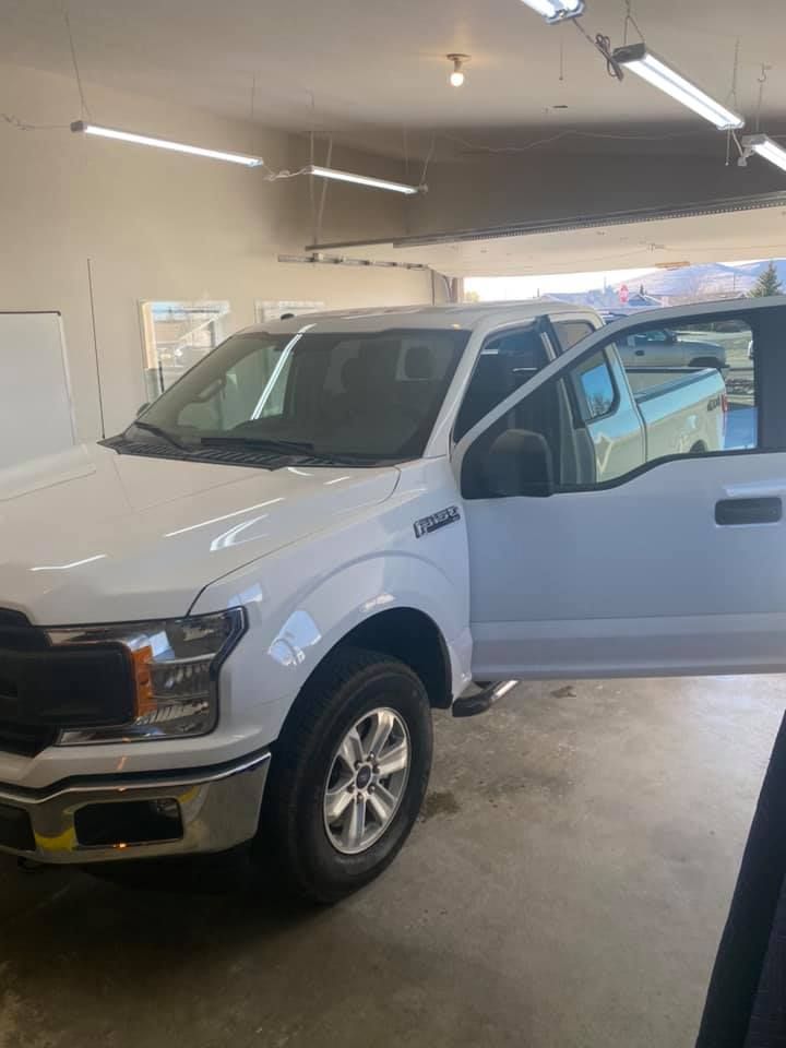 White Ford F-150 truck parked inside a garage, driver's side door open. Sunlight shines on the vehicle.