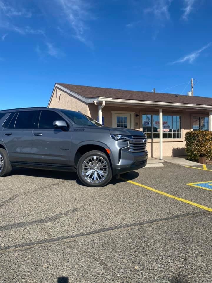 A gray SUV parked in front of a tan building under a blue sky.