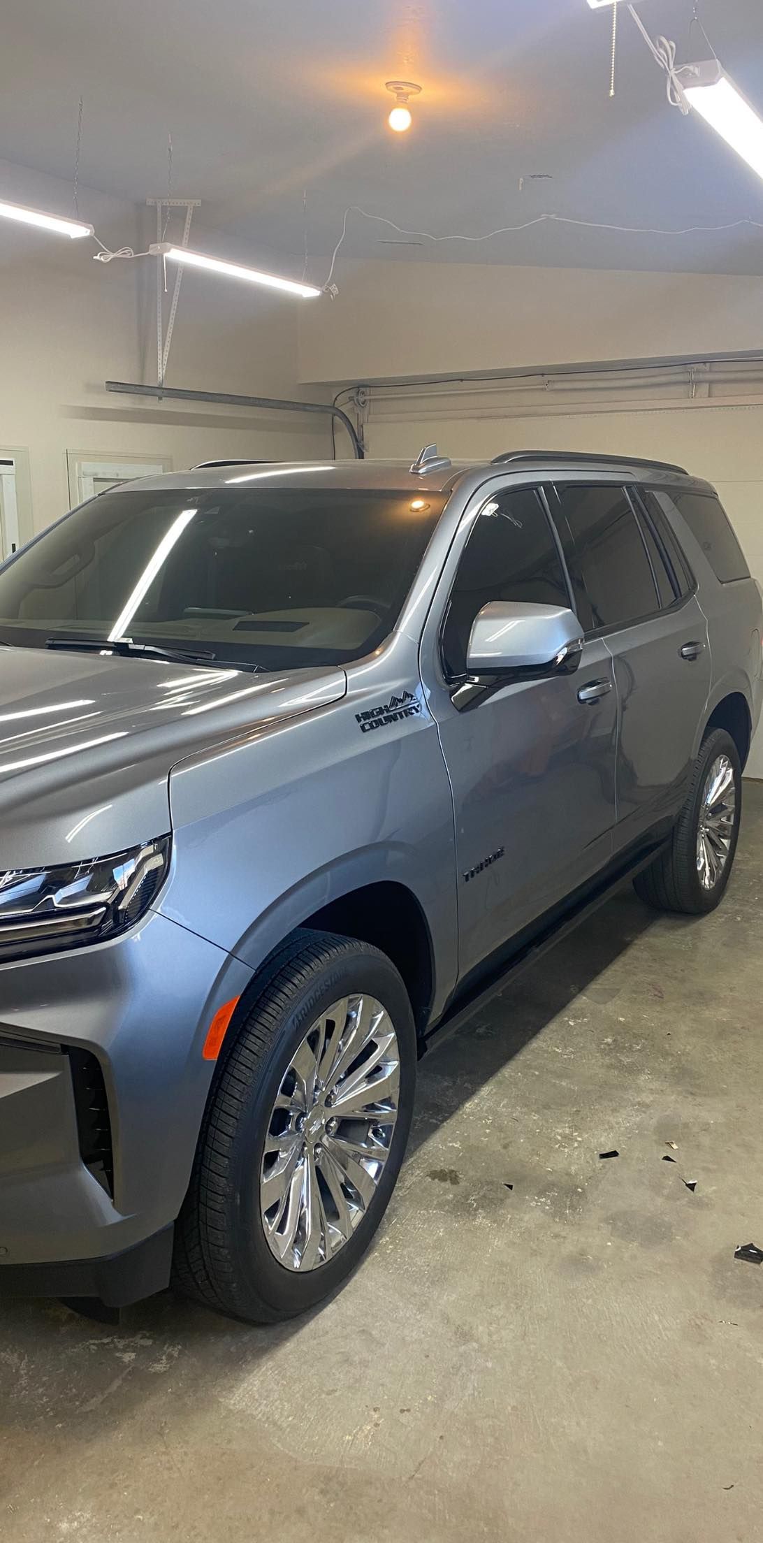 A gray SUV parked in a garage. It has tinted windows and chrome wheels. The vehicle is lit by overhead lights.