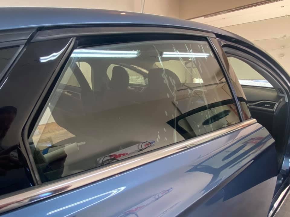 A blue car with a side window being tinted; the tinting film is visible on the glass.