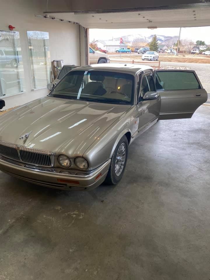 A tan Jaguar sedan with an open door, parked inside a garage.