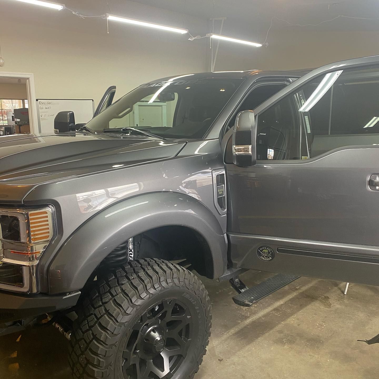 Gray pickup truck with black wheels and tinted windows, parked in a garage with the door open.