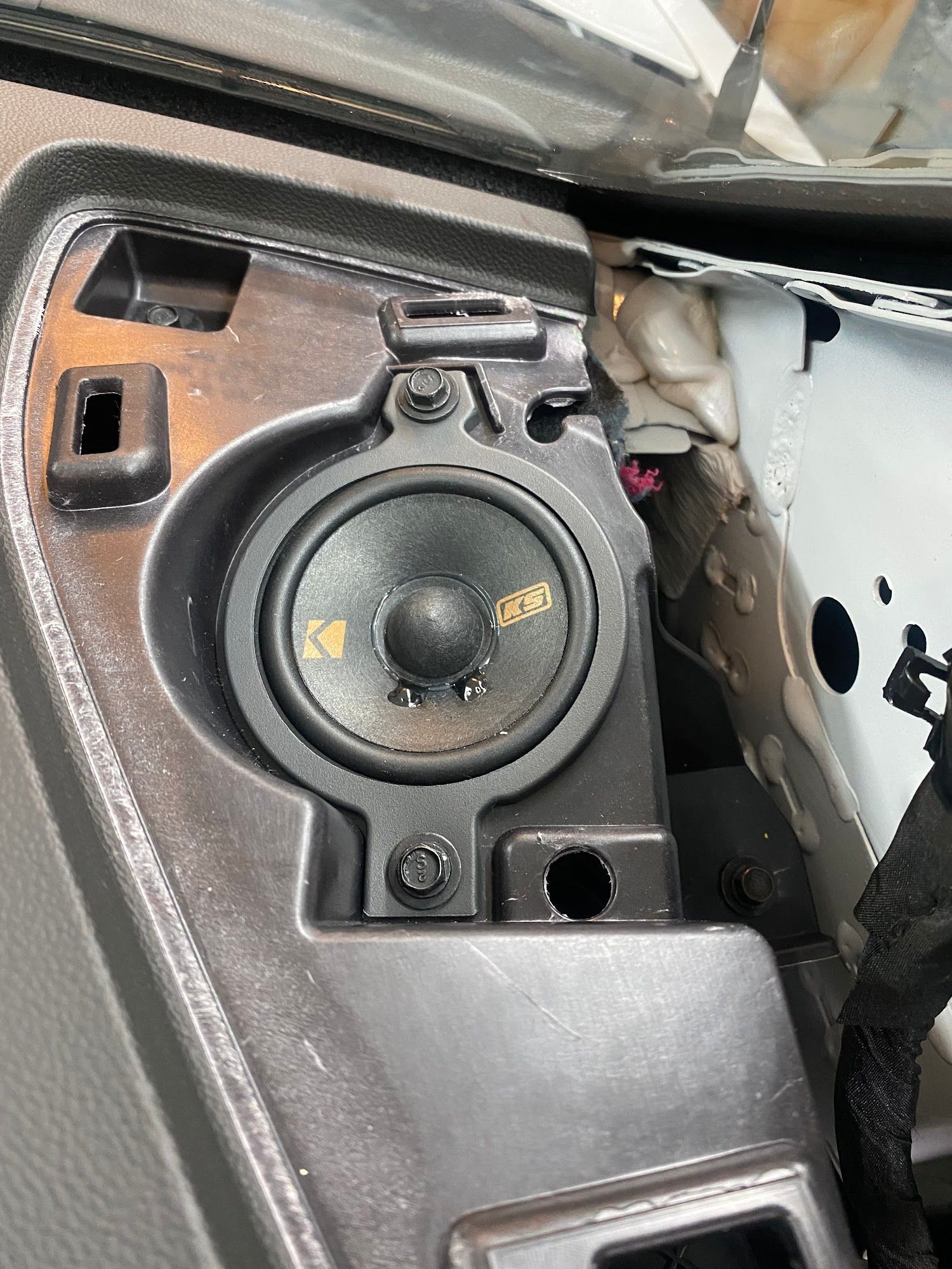 A dashboard speaker, a Kicker brand, is mounted within a car's dashboard. Black and gray interior.
