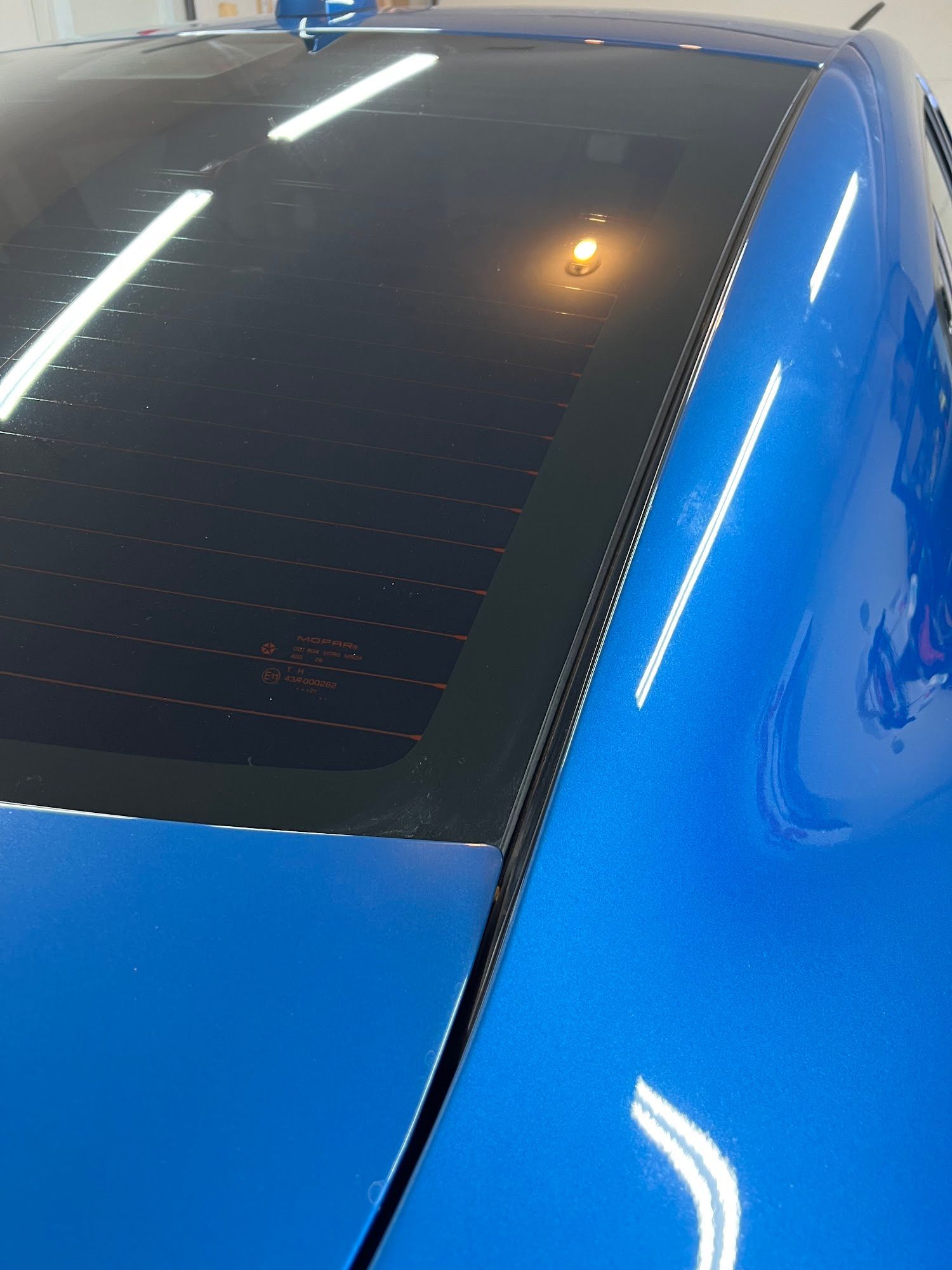 Blue car's rear window and roof, with visible defroster lines on the tinted glass. The car has a shiny finish.