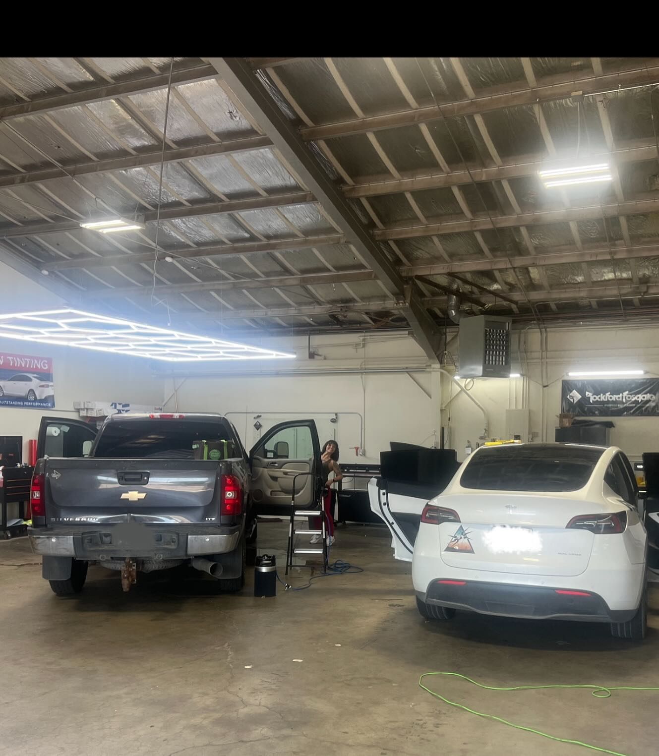 A garage interior with a gray pickup truck and a white Tesla. A person is near the open door of the pickup.